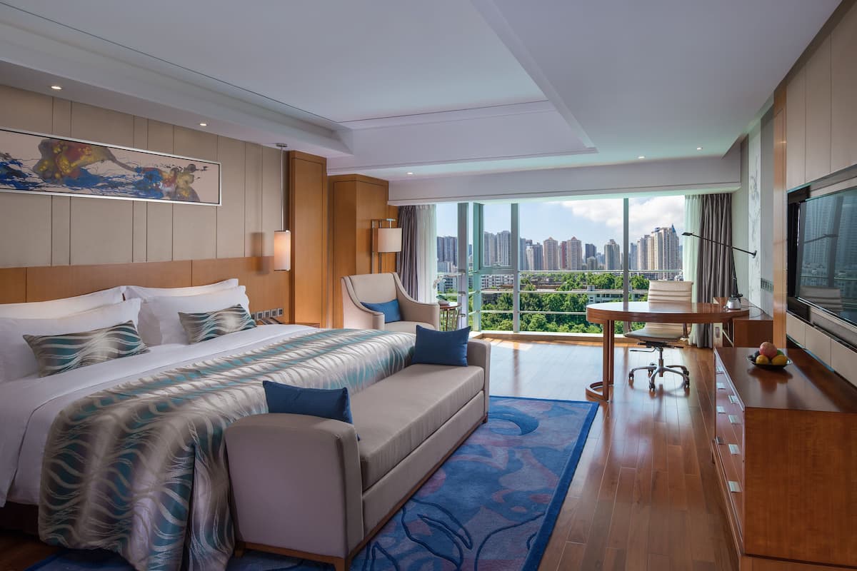 Une chambre d’hôtel moderne dotée d’un grand lit, d’un canapé, d’une table à manger et offrant une vue sur la ville grâce à de grandes fenêtres.