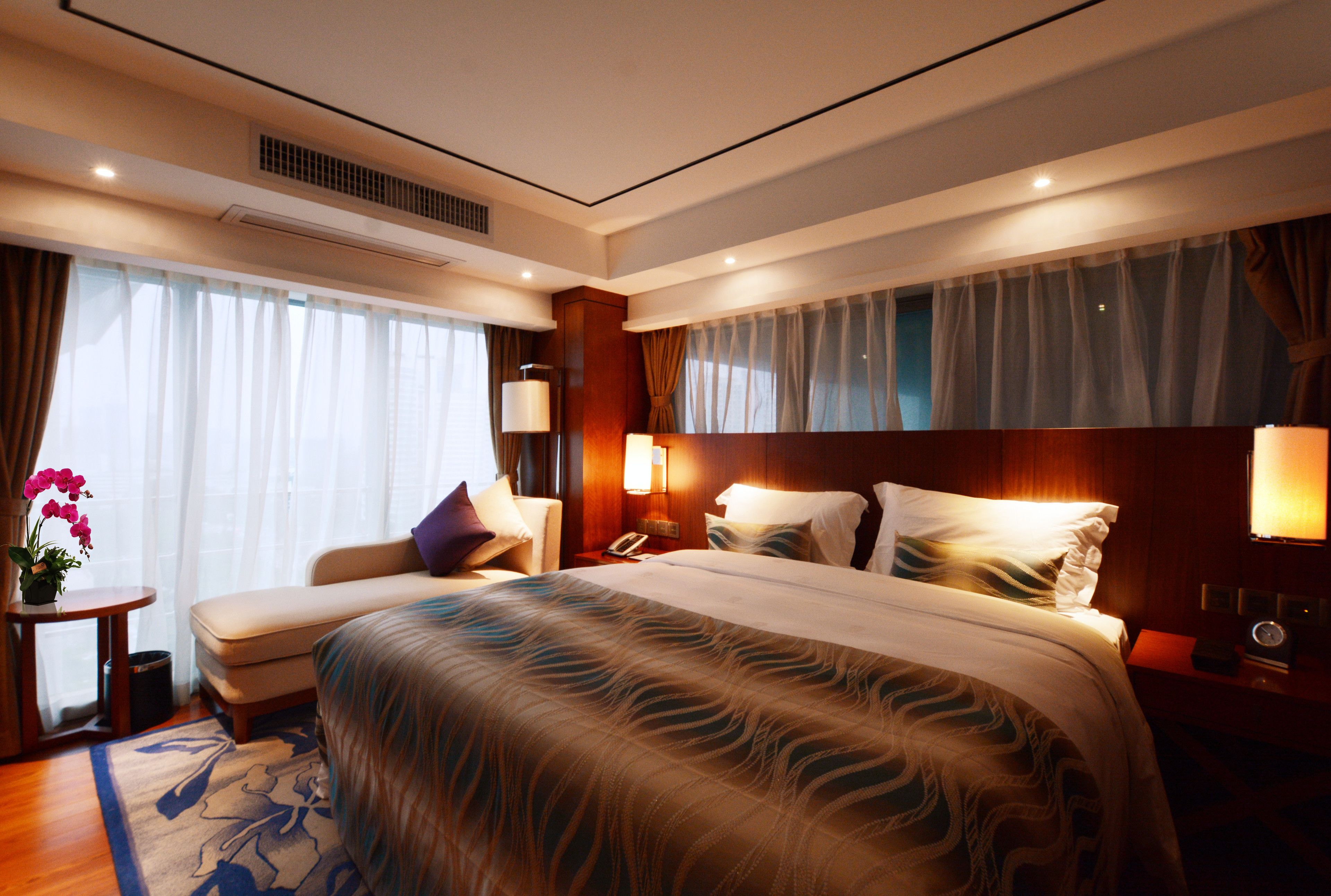 A hotel room with a large bed, a bedside table, a lamp, and a window with curtains.