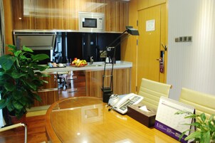 A hotel room with a wooden floor, a desk with a telephone, a calendar, and a plant.