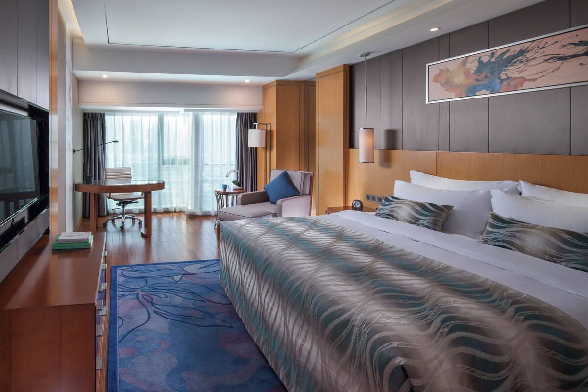 Une chambre d’hôtel avec un grand lit, un bureau, une chaise, une télévision et une fenêtre avec des rideaux.
