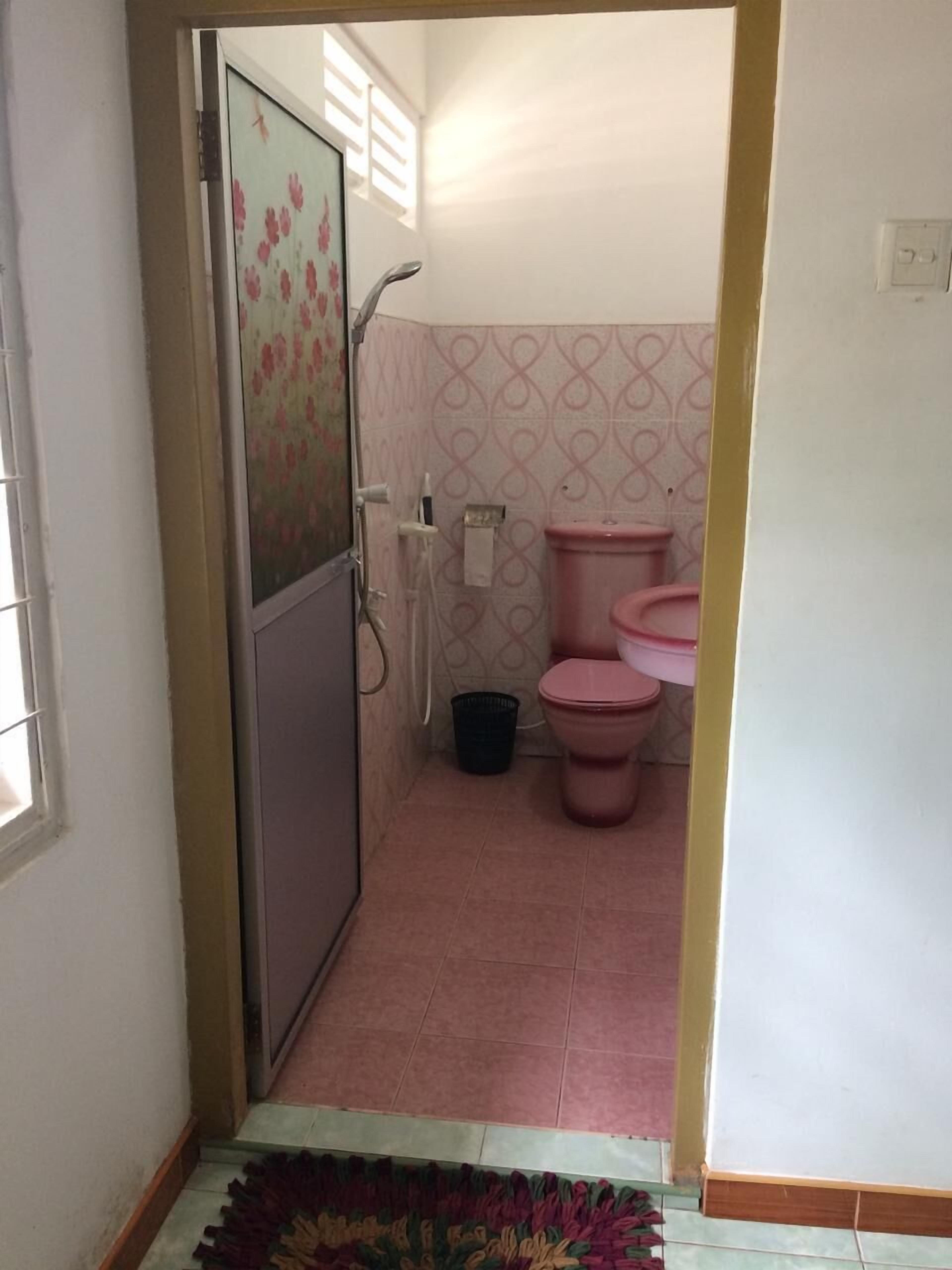 A bathroom with a shower, toilet, and a small trash bin.