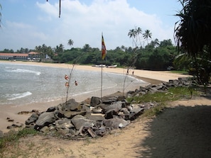 A beach with a rocky shoreline, palm trees, and a flagpole with a flag. - White Villa (Bentota)