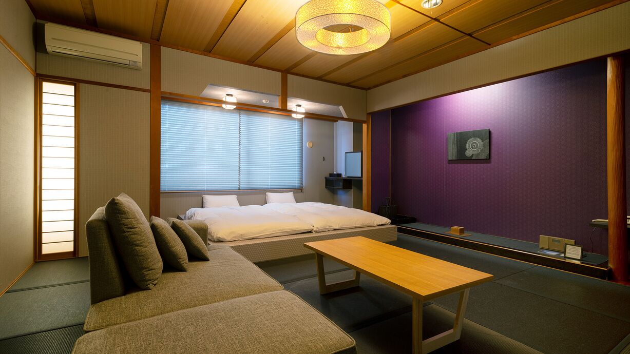Een traditionele Japanse kamer met tatami vloeren, een laag bed, een sofa, een houten tafel en een paarse accentmuur.