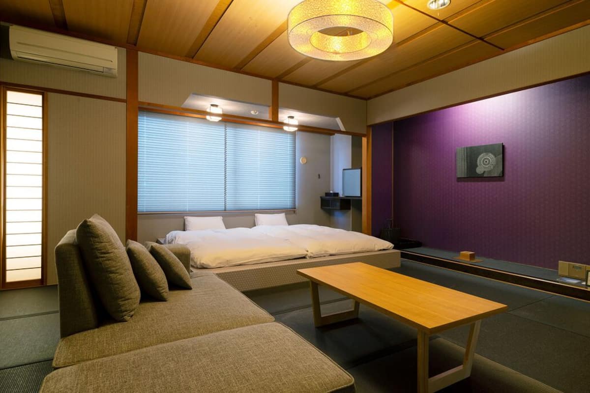 Una habitación tradicional japonesa con suelo de tatami, una cama baja, un sofá, una mesa de madera y una pared de acento morada.