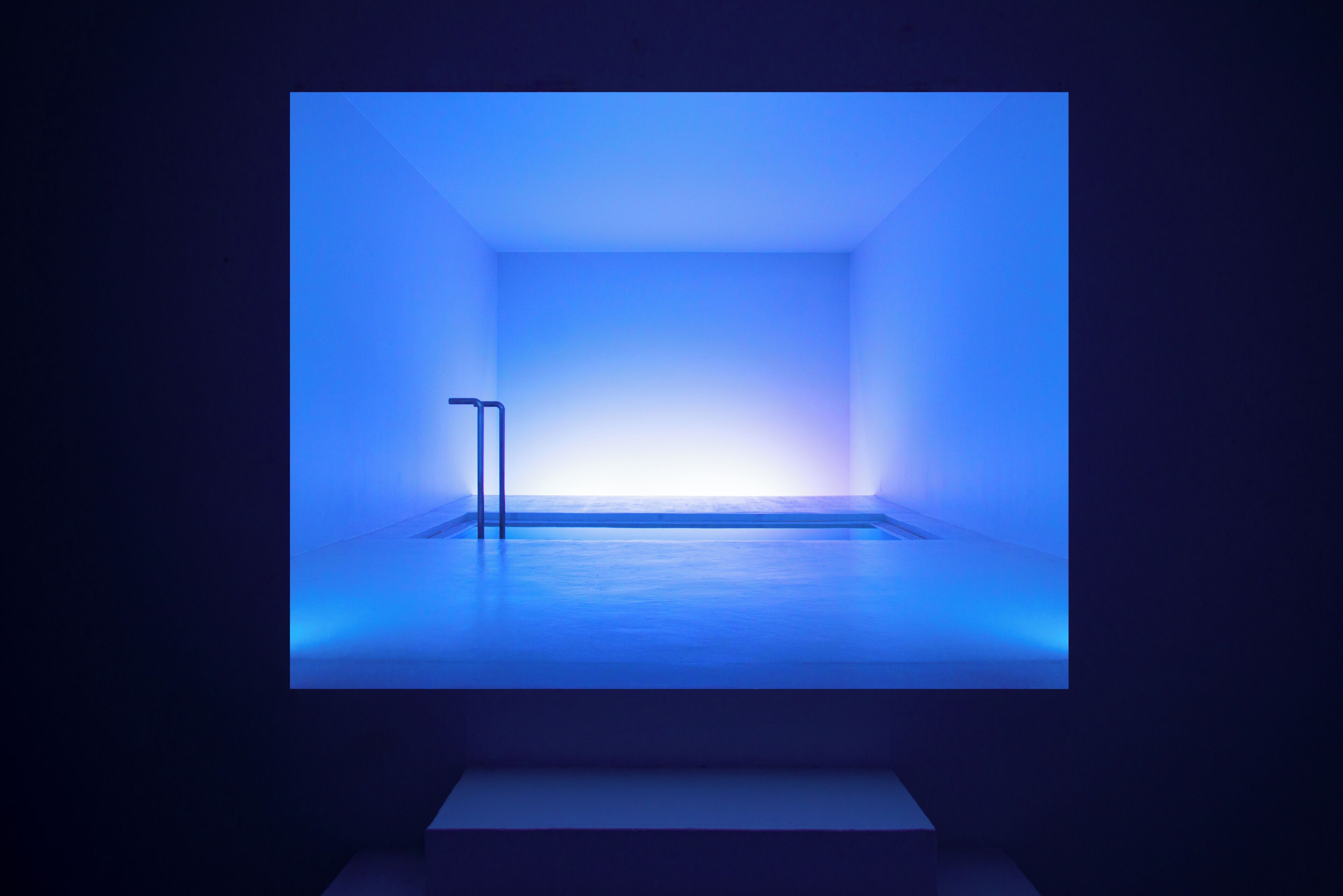 Una habitación minimalista con un ambiente azulado, una puerta visible y un suelo limpio y despejado.