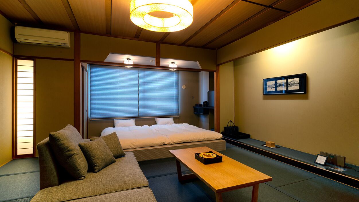 Een traditionele Japanse kamer met tatami vloerbedekking, een laag bed, een sofa, een houten tafel en een schuifdeur.