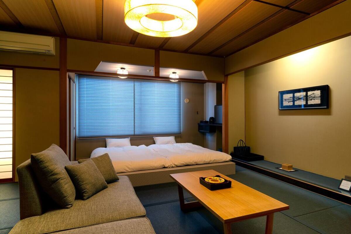 Une pièce de style japonais traditionnel, avec un sol recouvert de tatamis, un lit bas, un canapé, une table en bois et une porte coulissante.
