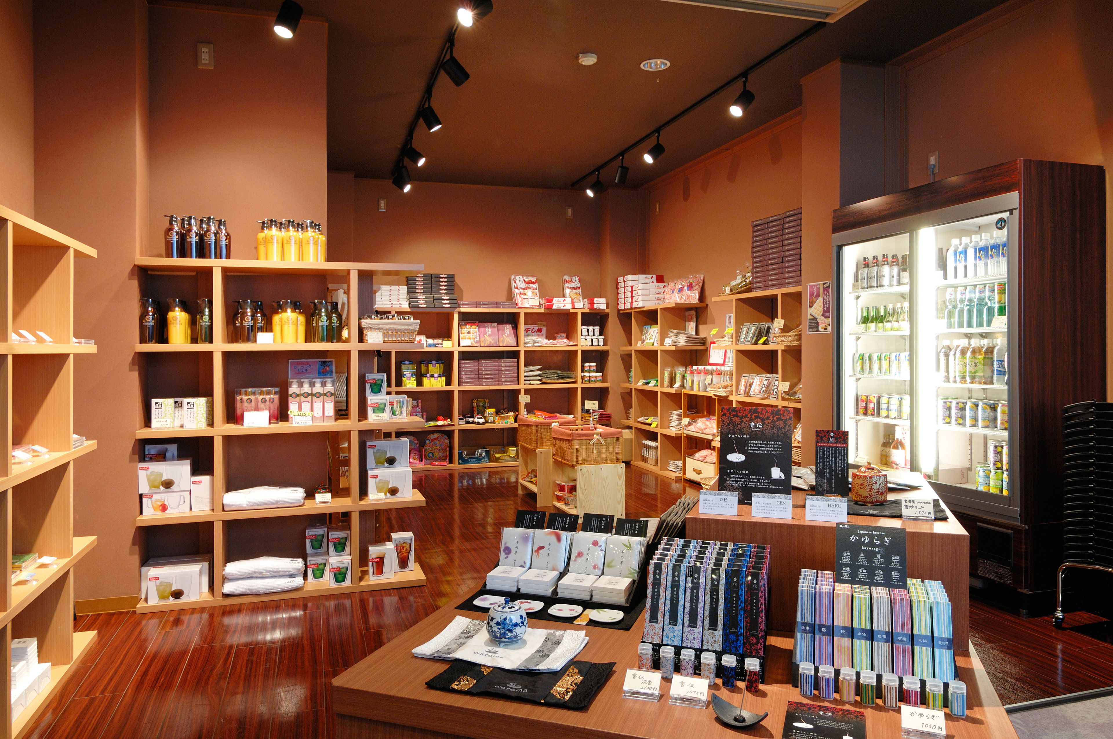 Una tienda con estantes de madera llenos de diversos productos, una mesa expositora con artículos y un refrigerador con bebidas.