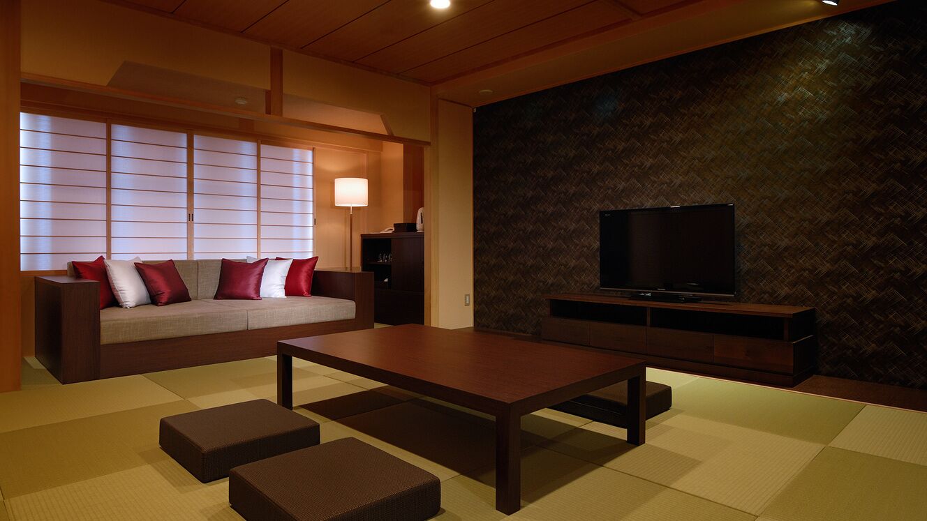 Een moderne woonkamer met een bank, een salontafel, tatami matten, een televisietoestel en een muur met een geometrisch patroon.