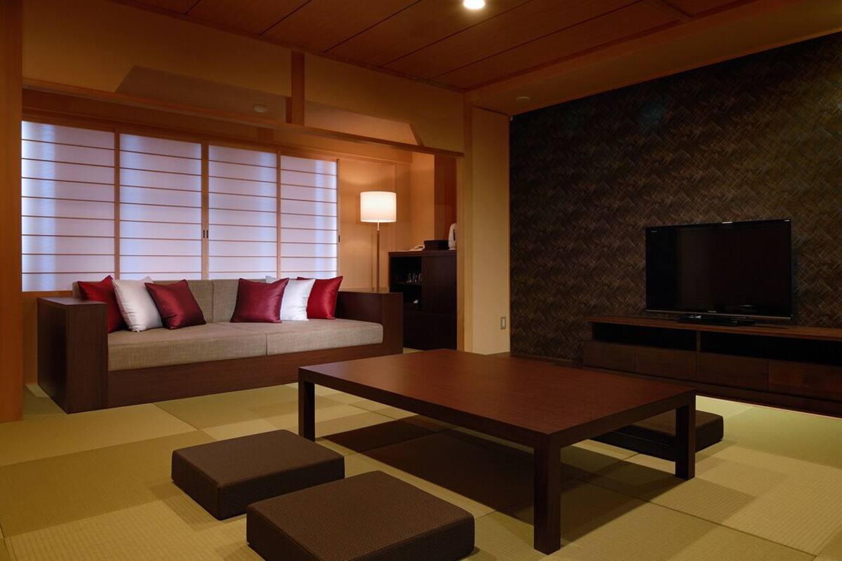 Un salon moderne comprenant un canapé, une table basse, des tatamis, un téléviseur et un mur orné d’un motif géométrique.