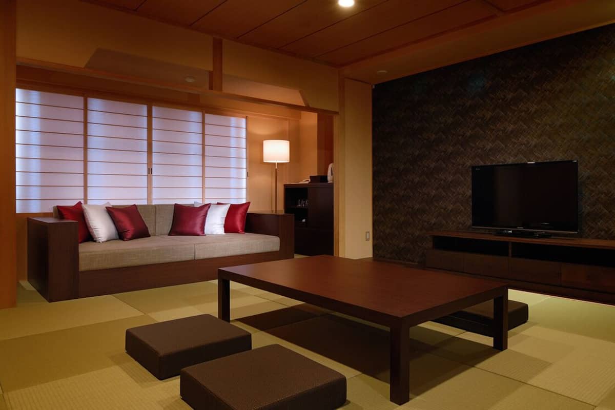Una sala de estar moderna con un sofá, una mesa de centro, esteras de tatami, un televisor y una pared con un diseño geométrico.