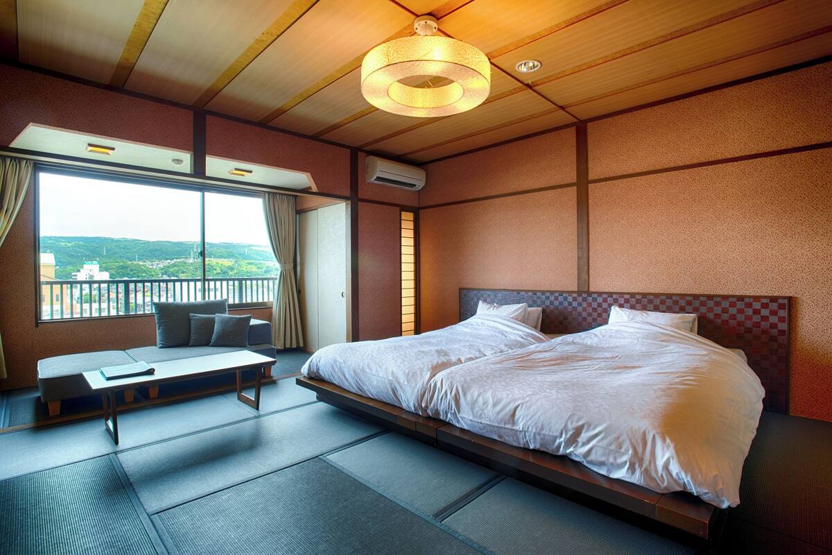 Une chambre d’hôtel avec un grand lit, un canapé, une vue sur la ville et un plafond en bois.