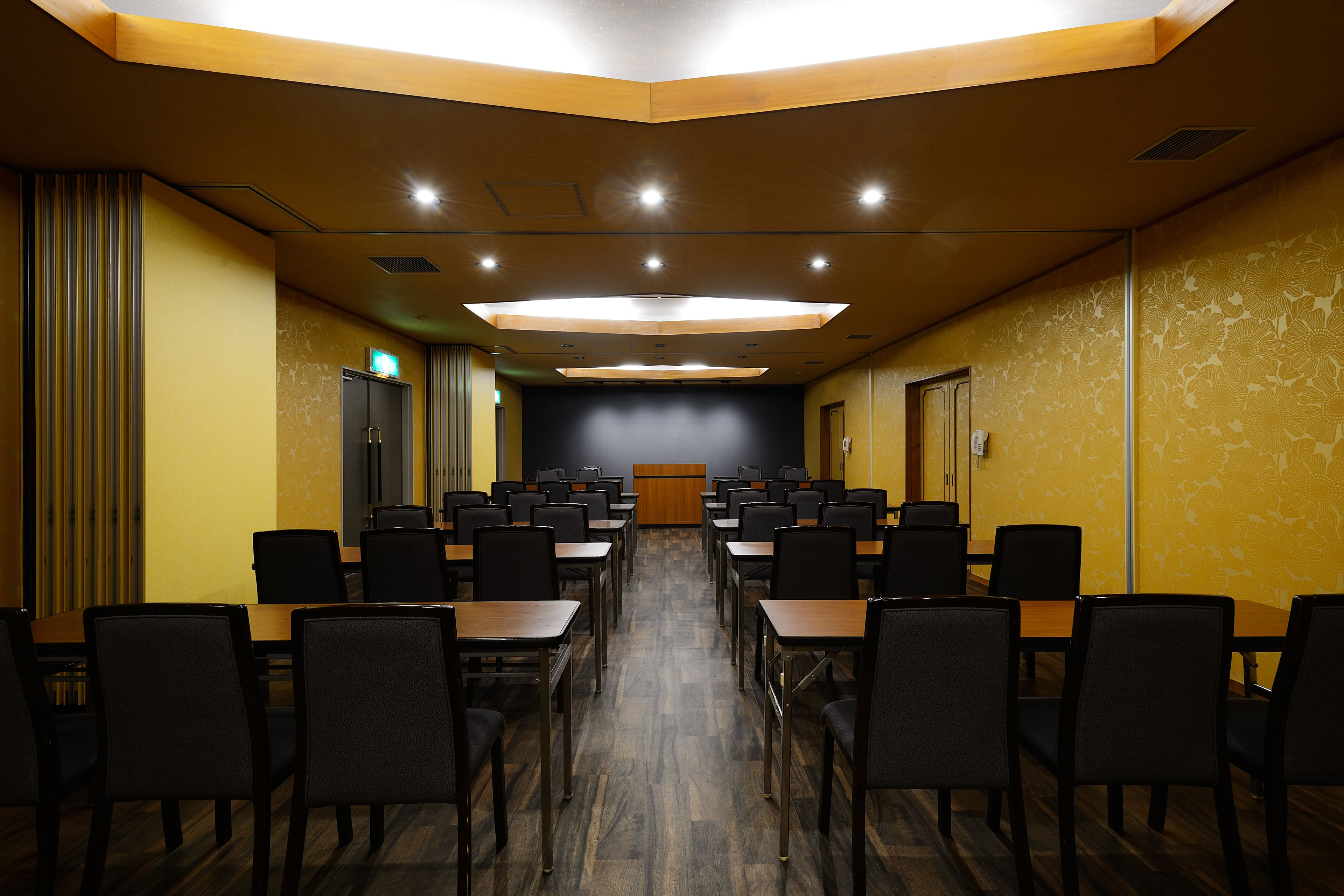 Un salón de conferencias con mesas y sillas dispuestas en filas, un atril al frente y un papel tapiz decorado en una pared.