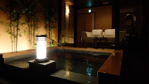 Een traditionele Japanse kamer met een kleine fontein, bamboepotten en een zithoek met witte kussens.