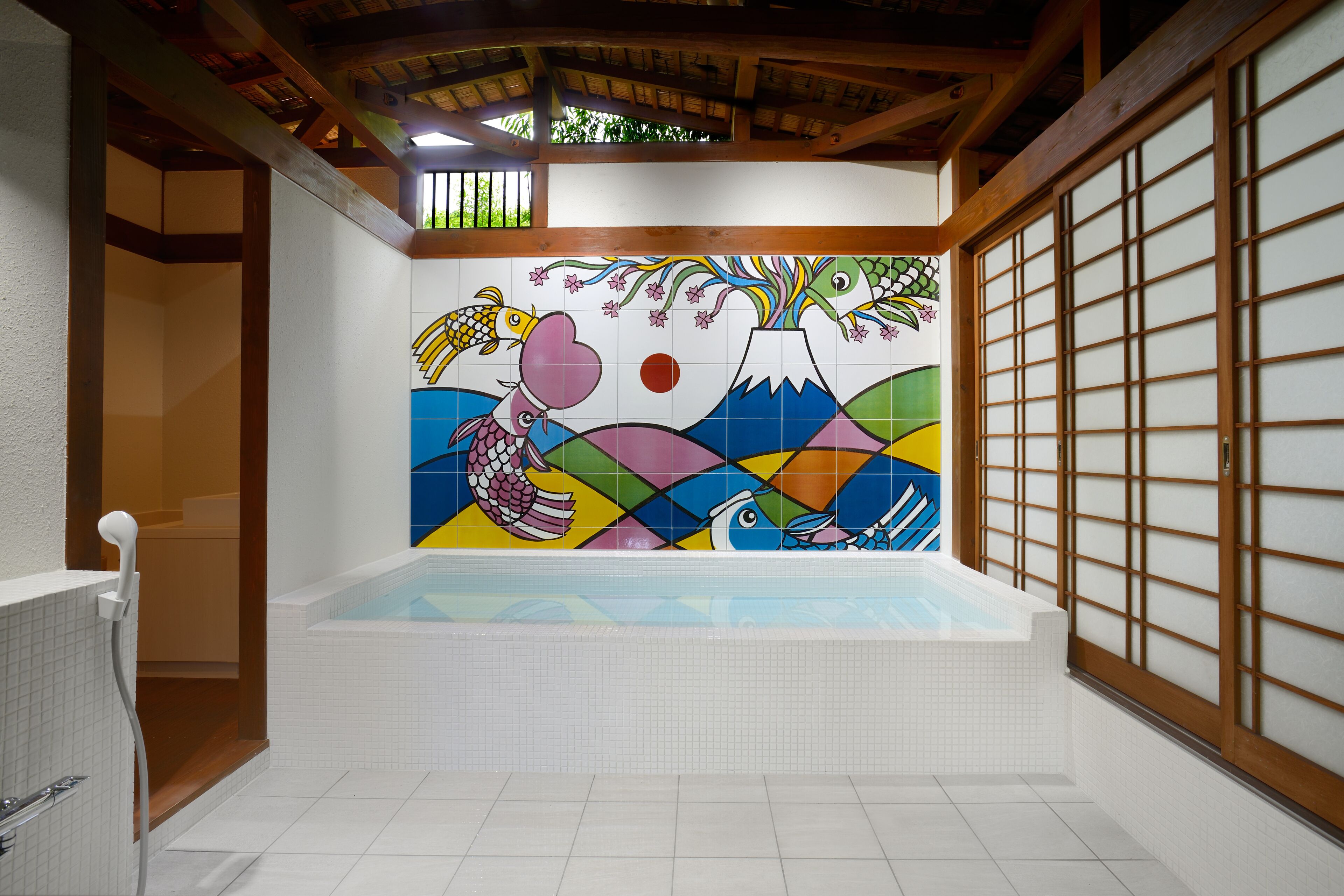 Una habitación tradicional japonesa con una bañera grande, puertas correderas de madera y un mural colorido en la pared.