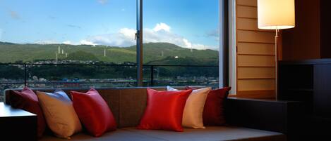 A modern room with a large window, a sofa with red and beige cushions, and a floor lamp.