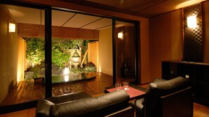 Een traditionele Japanse kamer met tatami vloeren, een lage tafel met kussens en uitzicht op een tuin door een schuifdeur.
