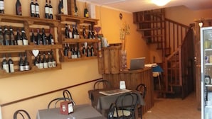 A dining area with a table and chairs, a wine rack with bottles, and a staircase leading to another level. - Ristoro Saint Roch (Hone)