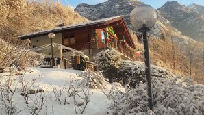 A wooden chalet with a balcony, surrounded by snow-covered vegetation and mountains in the background. - Ristoro Saint Roch (Hone)