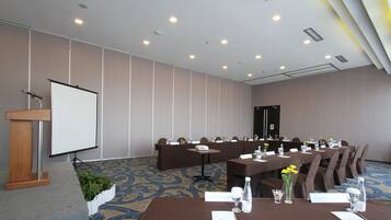 Un salón de conferencias con un atril, una pantalla de proyección y una larga mesa con sillas.