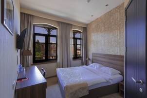 Una habitación de hotel con cama, escritorio, televisor y ventana con cortinas.