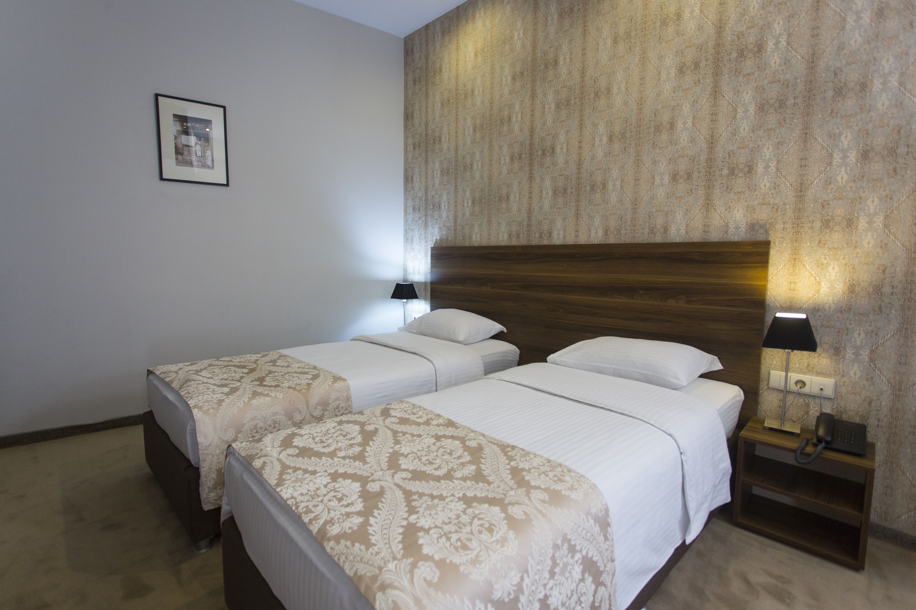A hotel room with two beds, a nightstand with a lamp, and a framed picture on the wall.