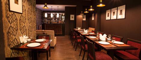 Un restaurante con varias mesas, sillas con cojines rojos y lámparas colgantes.