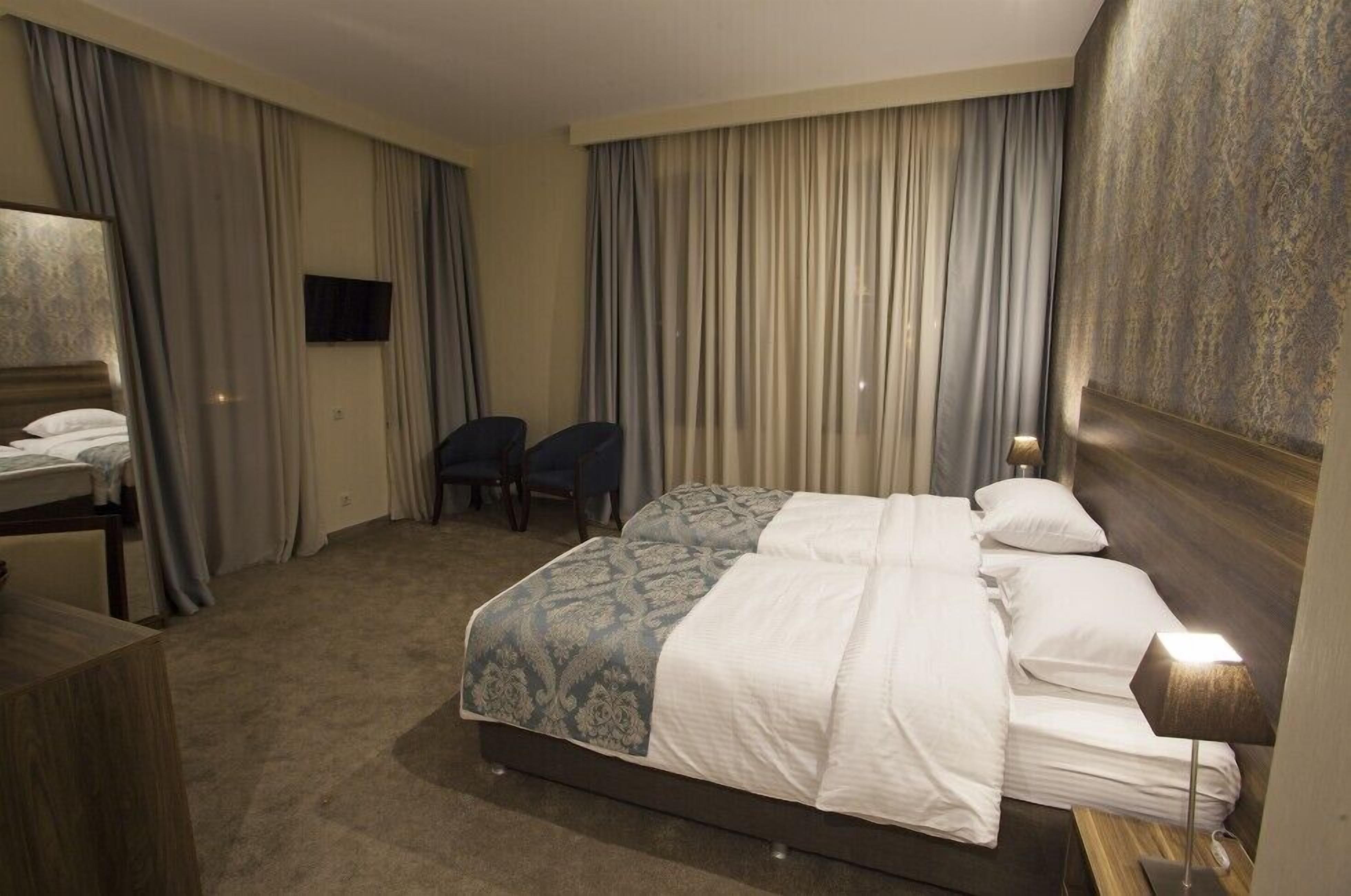 Et hotelværelse med en stor seng, et skrivebord, en stol og et fjernsyn på væggen.