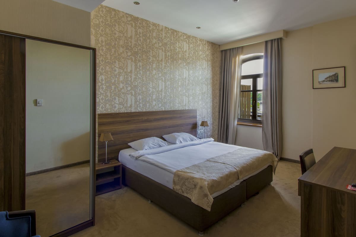 A hotel room with a large bed, a desk, a chair, a lamp, and a window with curtains.