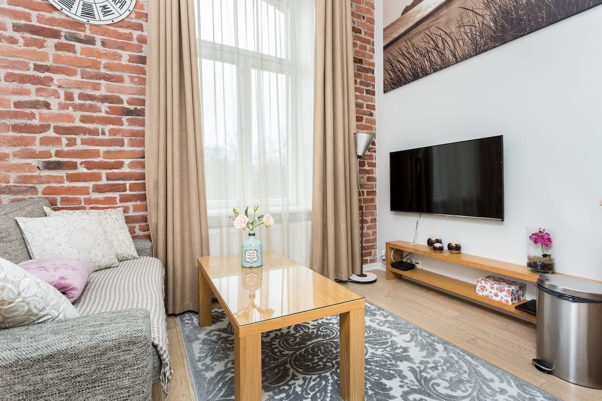 Ein Wohnzimmer mit Backsteinwand, einer Couch, einem Couchtisch, einem Fernseher und einem Holzregal.