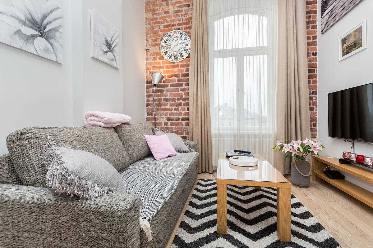 Ein modernes Wohnzimmer mit Backsteinwand, einer Couch, einem Couchtisch, einem Fernseher und einem Fenster mit Vorhängen.