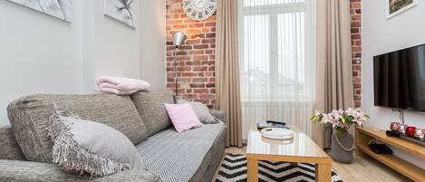 Un salon moderne avec un mur en briques, un canapé, une table basse, un téléviseur et une fenêtre avec des rideaux.