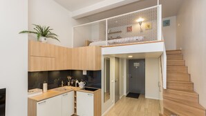 A modern kitchen with wooden cabinets, a sink, and a small refrigerator. There is a staircase leading to an upper level with a mesh railing. - Angleterre Apartments (Tallinn)