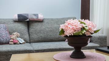 A living room with a grey sofa, a small table with a pink placemat, and a vase of pink flowers.