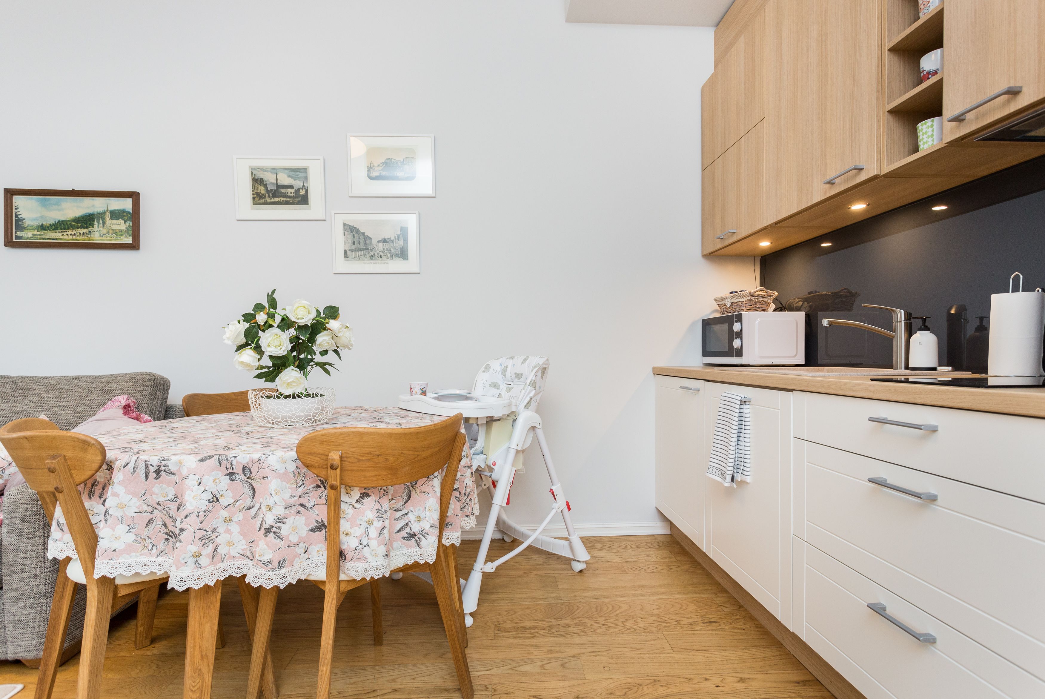 Una cocina compacta con armarios de madera, una mesa de comedor con mantel floral y una trona.