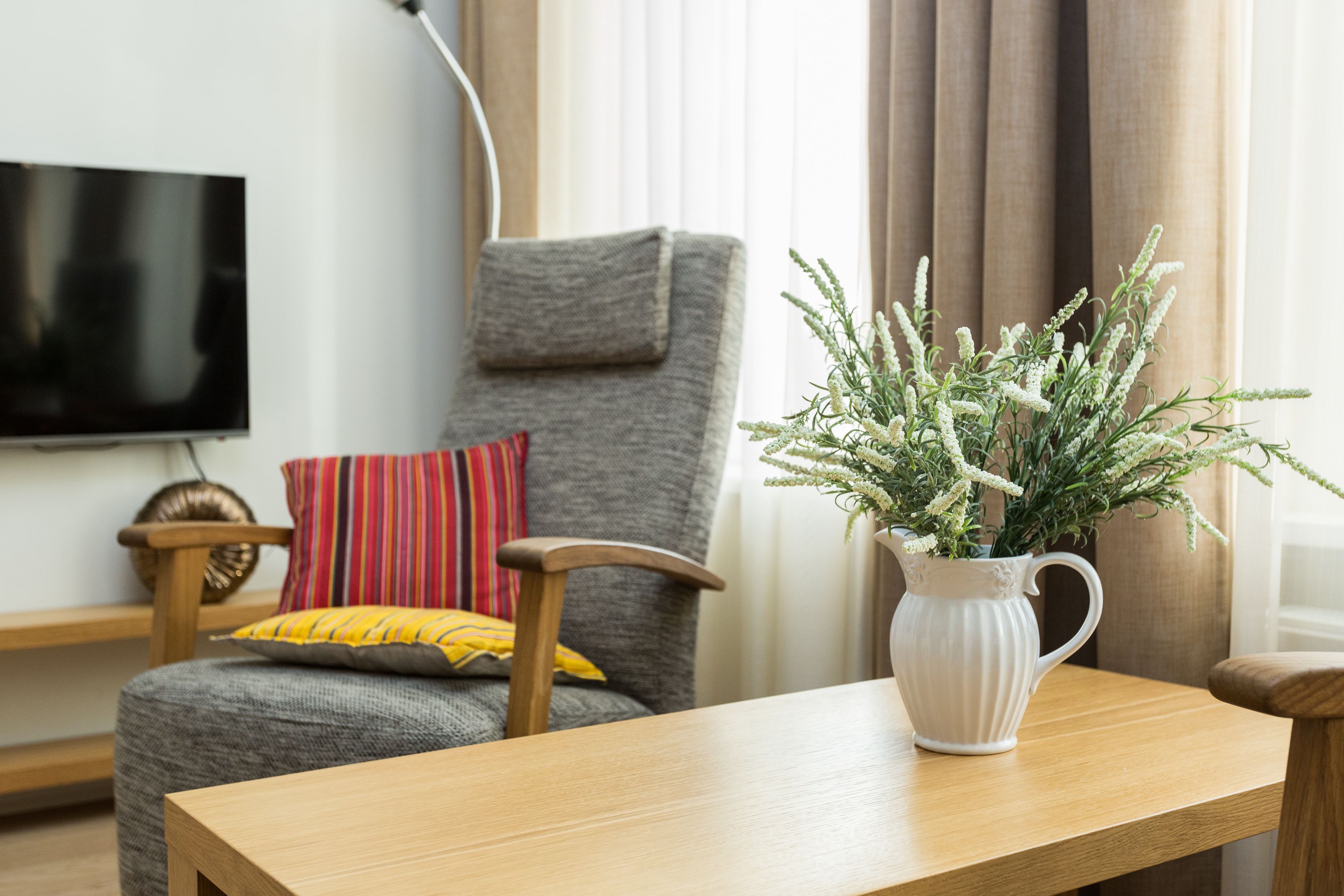 A living room with a grey armchair, a wooden coffee table, and a white vase with green plants.