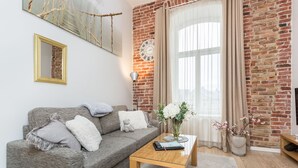 A living room with a grey sofa, a wooden coffee table, a vase with flowers, a clock on the wall, and a brick wall. - Angleterre Apartments (Tallinn)
