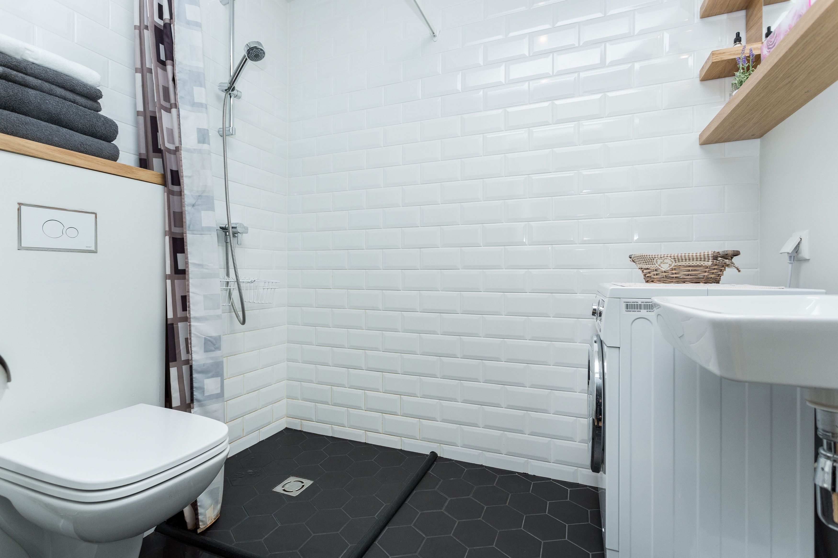 A modern bathroom with a white tiled shower, a white toilet, and a small sink.