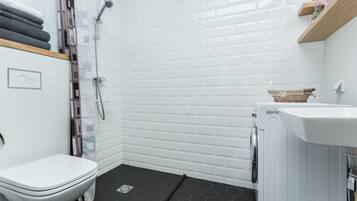 A modern bathroom with a white tiled shower, a white toilet, and a small sink.