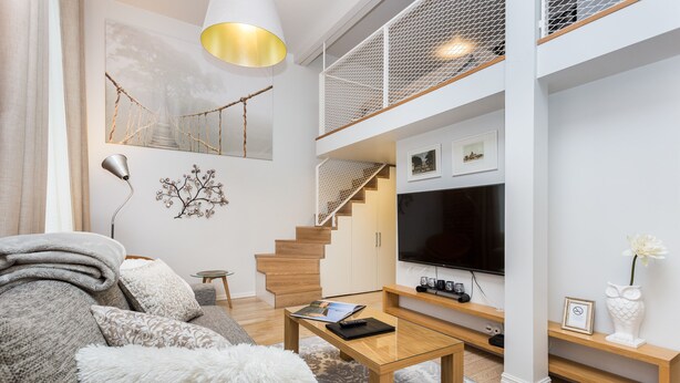 A modern living room with a sofa, coffee table, and a TV. There is a staircase with a railing, and a chandelier. - Angleterre Apartments (Tallinn)