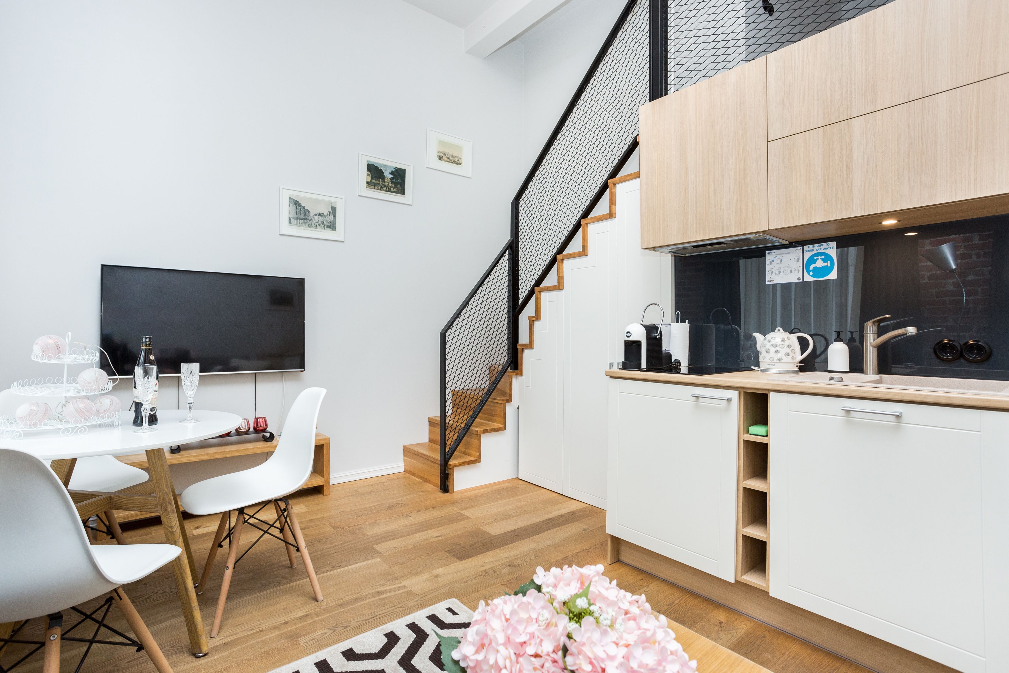 Una cucina moderna con mobili bianchi, una scala in legno e un televisore a schermo piatto.