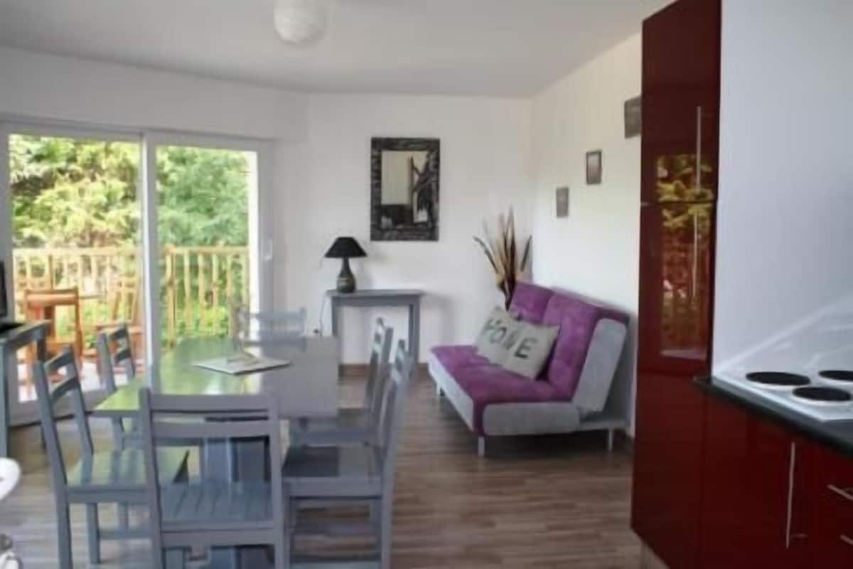 A modern kitchen with a dining area, a sofa with a 'FINE' pillow, and a view of the outdoors.