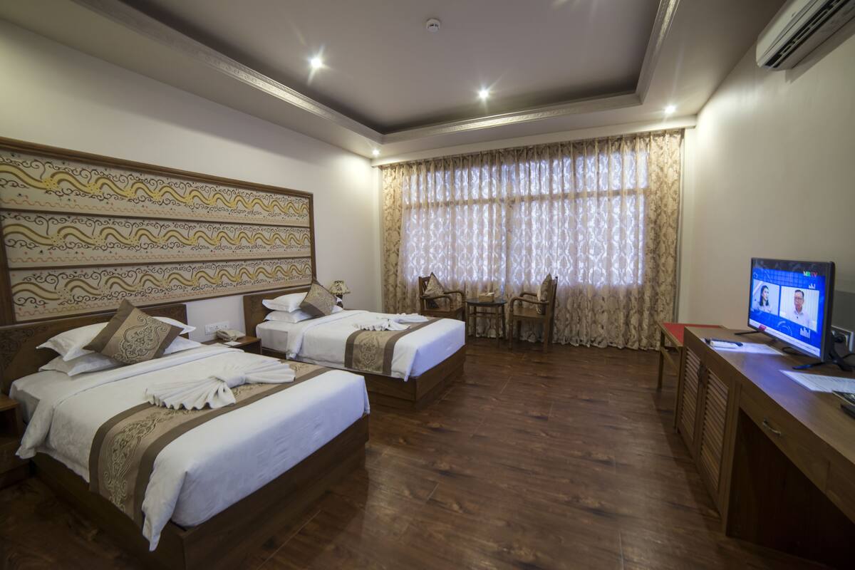 A hotel room with two beds, a desk, a chair, and a television.