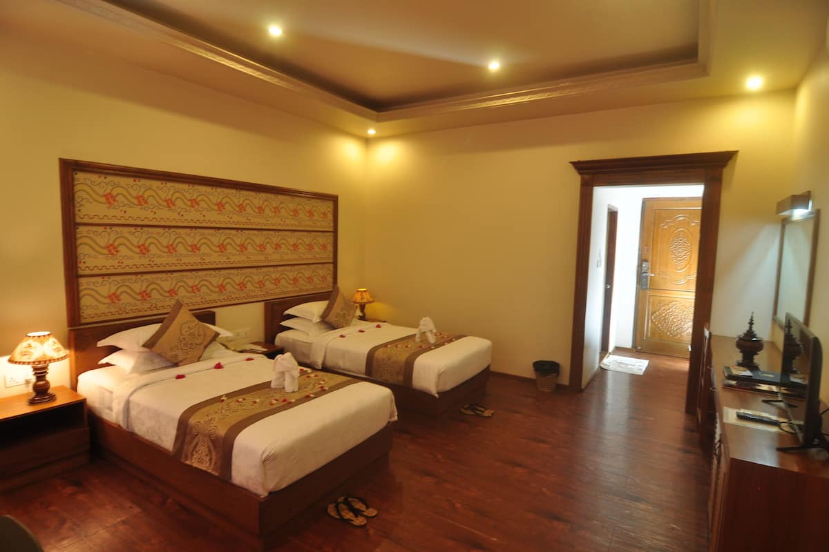 A hotel room with two beds, a nightstand, a lamp, a mirror, and a wooden floor.