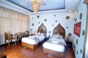 Habitación de hotel con dos camas, piso de madera, candelabro y decoración mural.