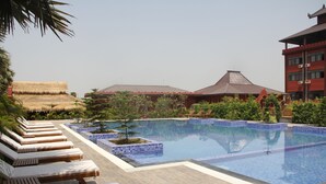 A swimming pool with lounge chairs and a building with a traditional roof in the background. - Gracious Bagan Hotel (Nyaung-U)