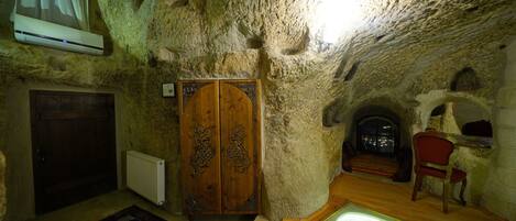Un intérieur qui rappelle une grotte, avec une porte en bois, un radiateur, un tapis à motifs et un espace délimité par des parois de verre.