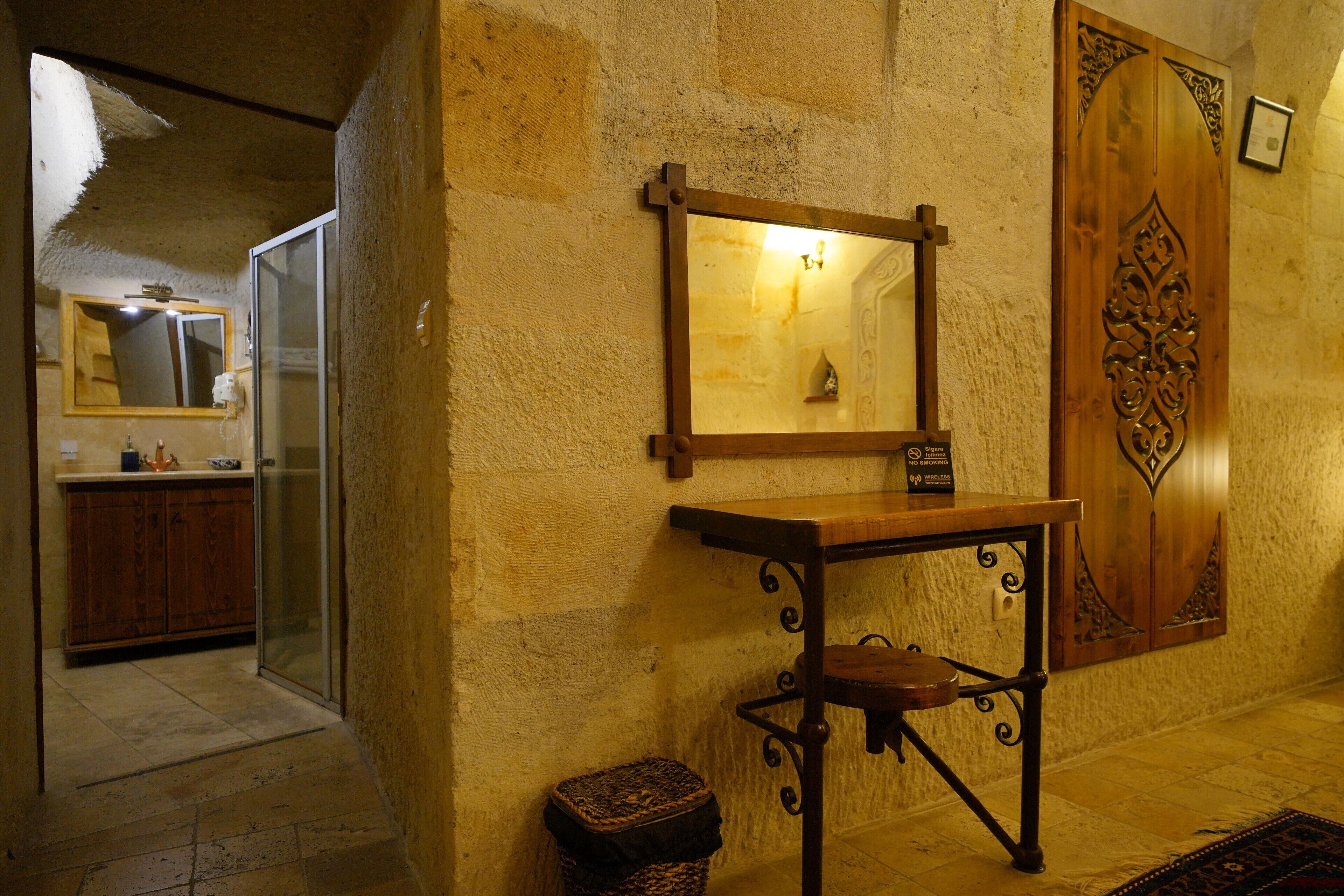 Una habitación con pared de piedra, puerta de madera con elaborados grabados, una mesa de madera con espejo y un pequeño cofre de madera.