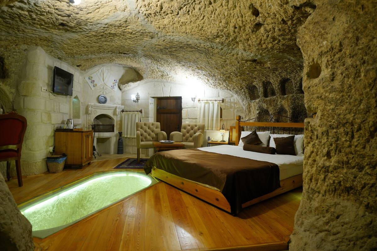 Ein Schlafzimmer mit Steindecke, einem Bett, Holzboden, einem kleinen Tisch, einem Sessel und einem an der Wand befestigten Fernseher.