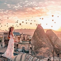 Una persona de pie en un balcón con vistas a un paisaje montañoso y edificios tradicionales.